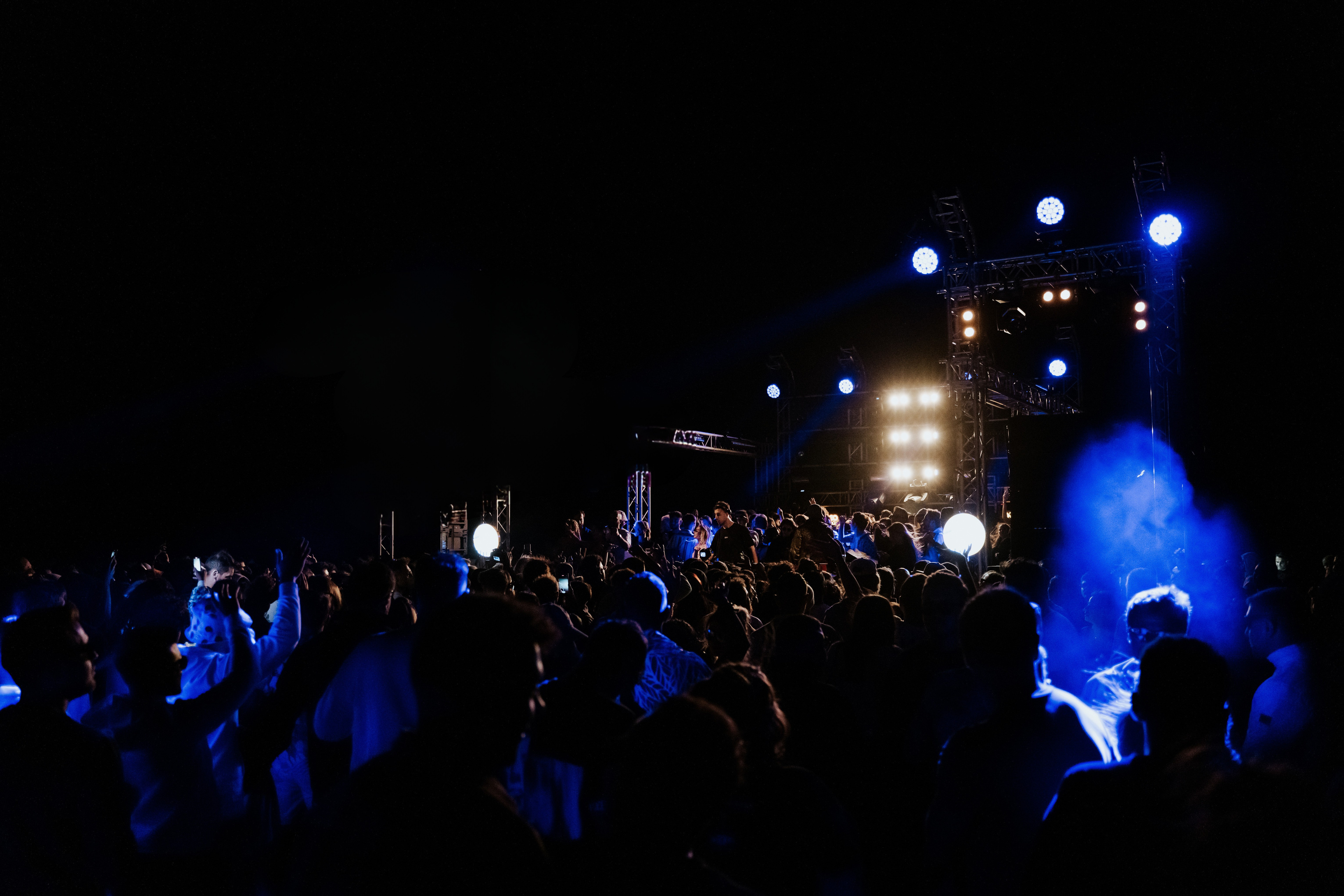 Open-air crowd in blue light facing the stage